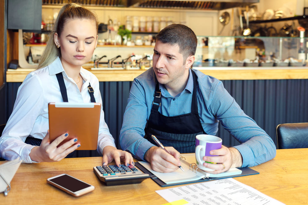 Paar sitzt über der Buchhaltung. für ihr Restaurant. Mit Taschenrechner und IPad