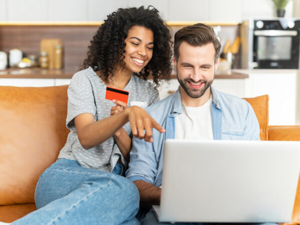 Woman with a credit card in her hand looks at a notebook together with a young man